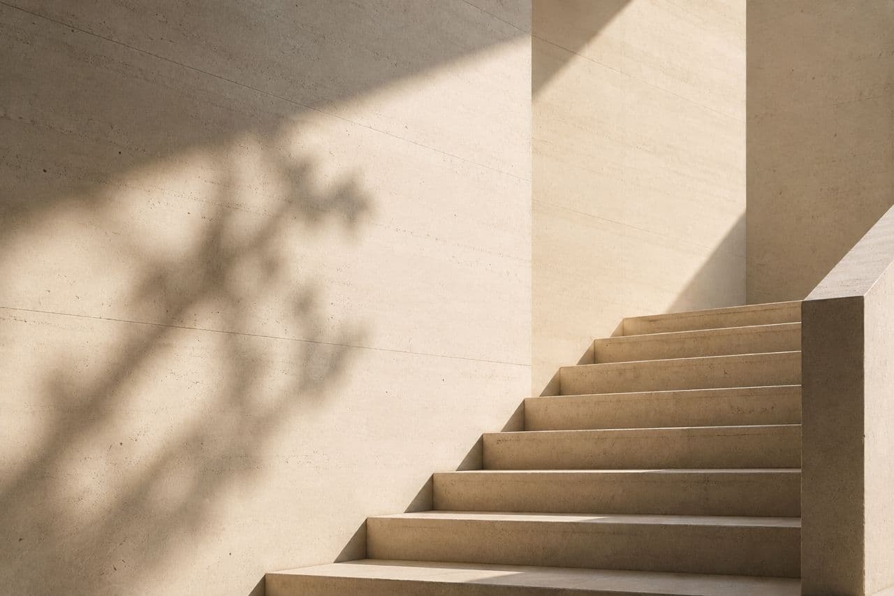 An ivory travertine staircase with the shadow of a tree cast across the wall behind it.